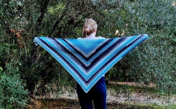 Aquamarine Joy Triangle Shawl — crochet shawl patterns Person wearing a blue and black striped crochet shawl outdoors — crochet shawl patterns