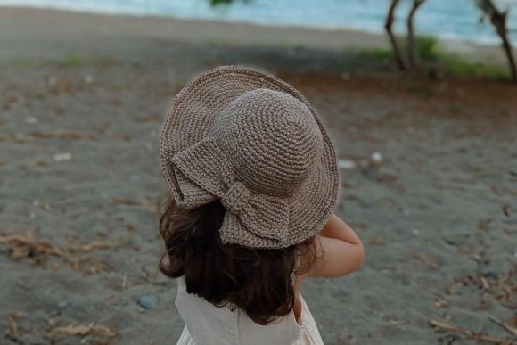 Crochet Coquette Sun Hat — crochet hat patterns for every season Crochet Coquette Sun Hat on a child by the beach — crochet hat patterns for every season