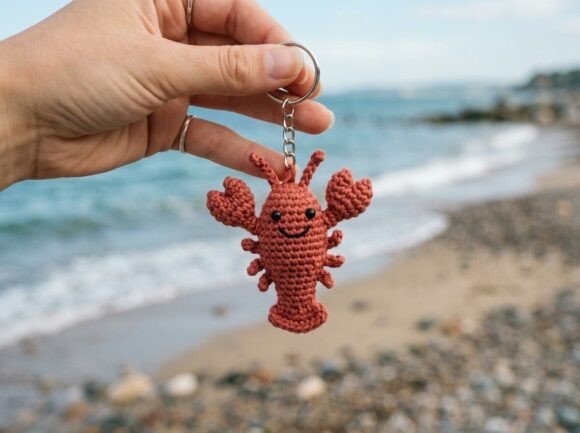 Crochet Lobster Keychain — crochet amigurumi keychain Crochet amigurumi keychain of a lobster held by a hand near the beach.